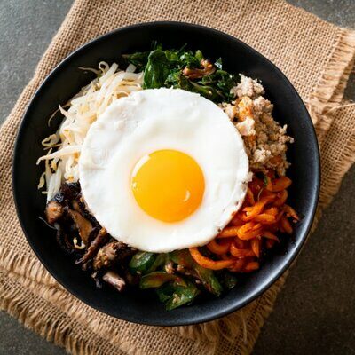 Bibimbap is a Korean dish made with a base of rice. White steamed rice, topped with sautéed vegetables known as namul, slices of meat (usually beef), and fried or raw egg all make up the dish.